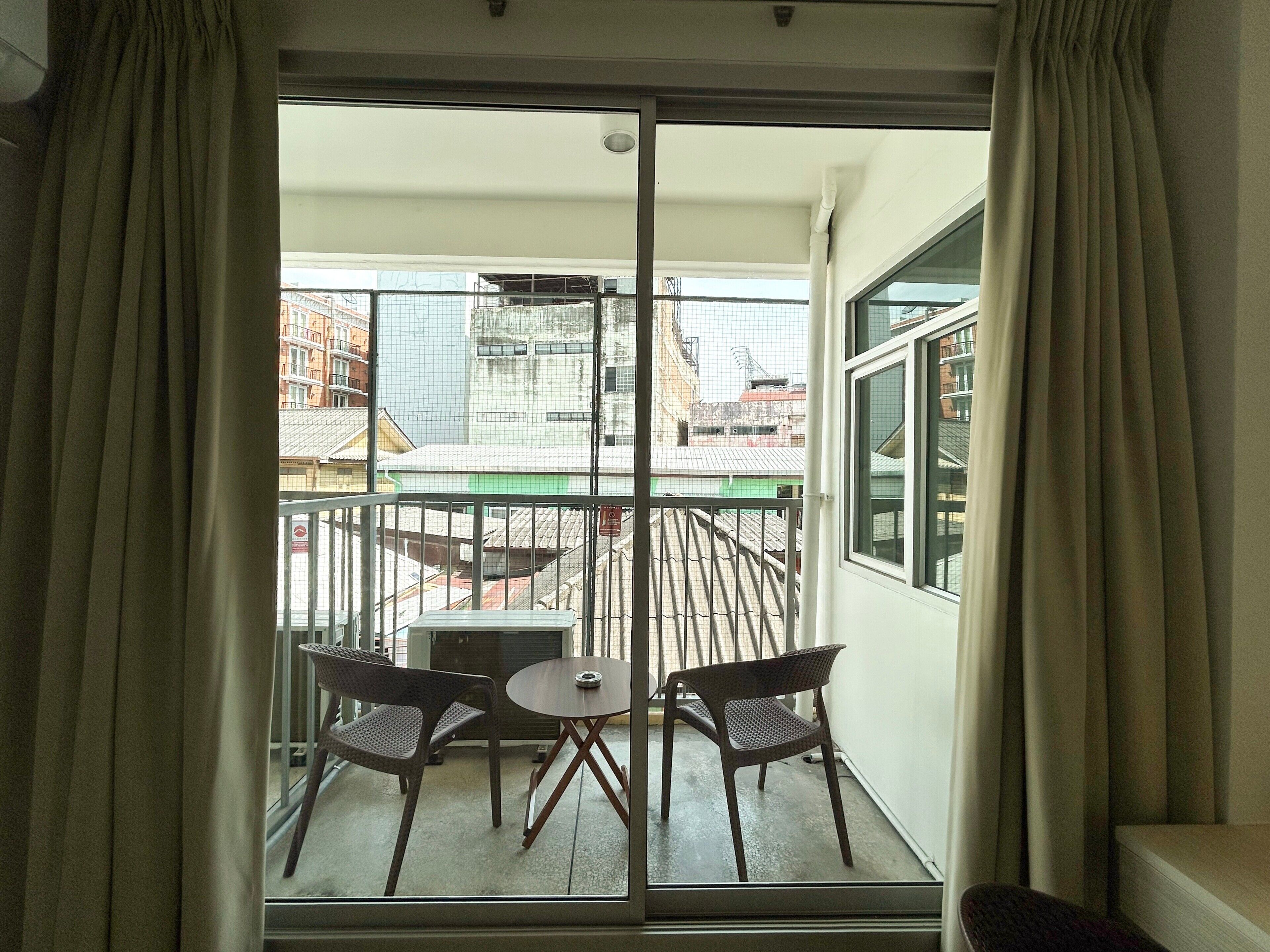 Un balcon avec une table et deux chaises, une vue sur les bâtiments et une porte-fenêtre coulissante.