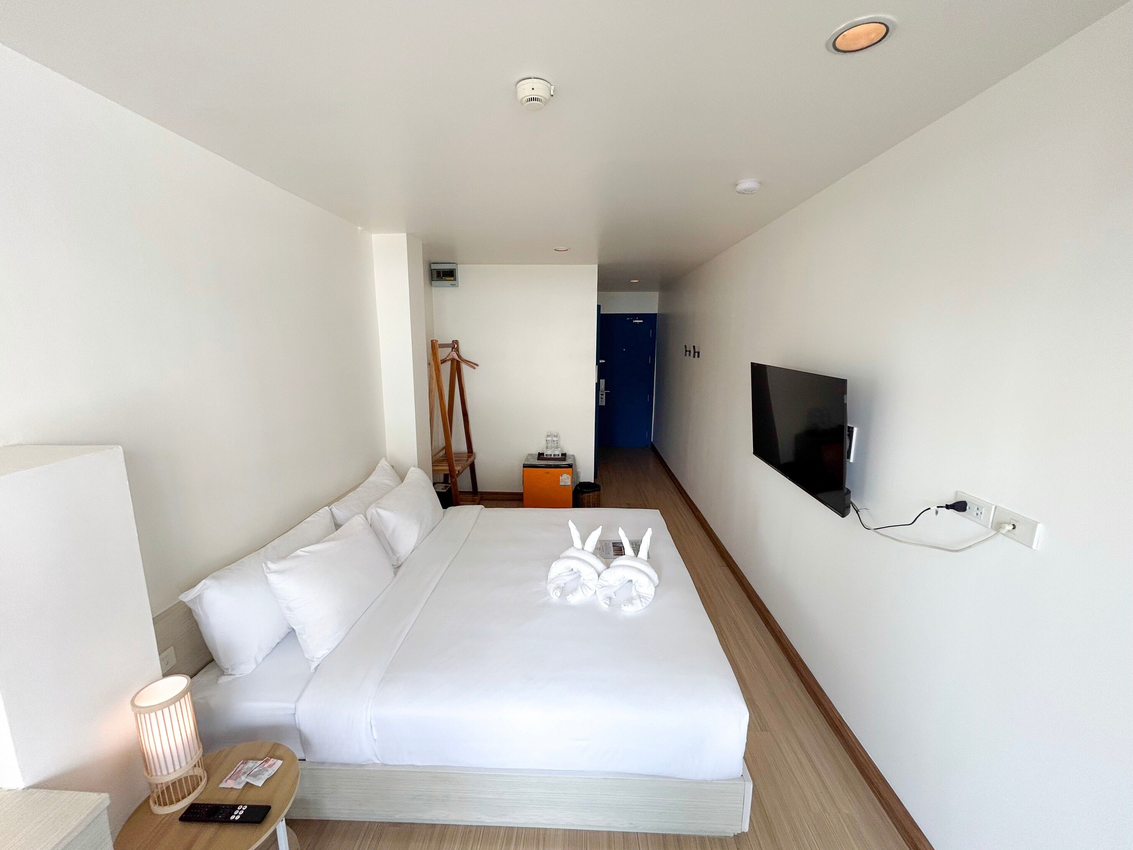 Een hotelkamer met een bed, een televisie, een nachtkastje met een lamp en een houten vloer.