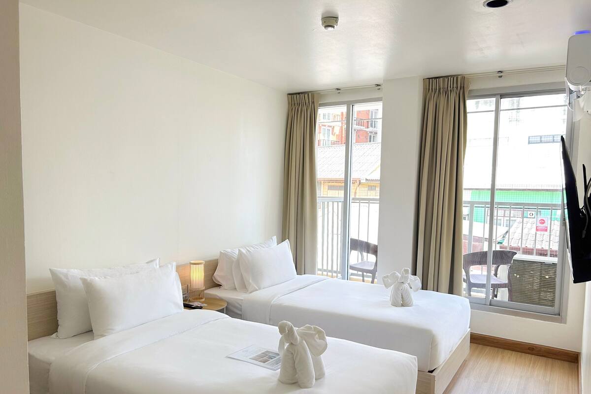 Une chambre d’hôtel avec deux lits, une fenêtre avec des rideaux, une table de chevet avec une lampe et une vue sur l’extérieur.