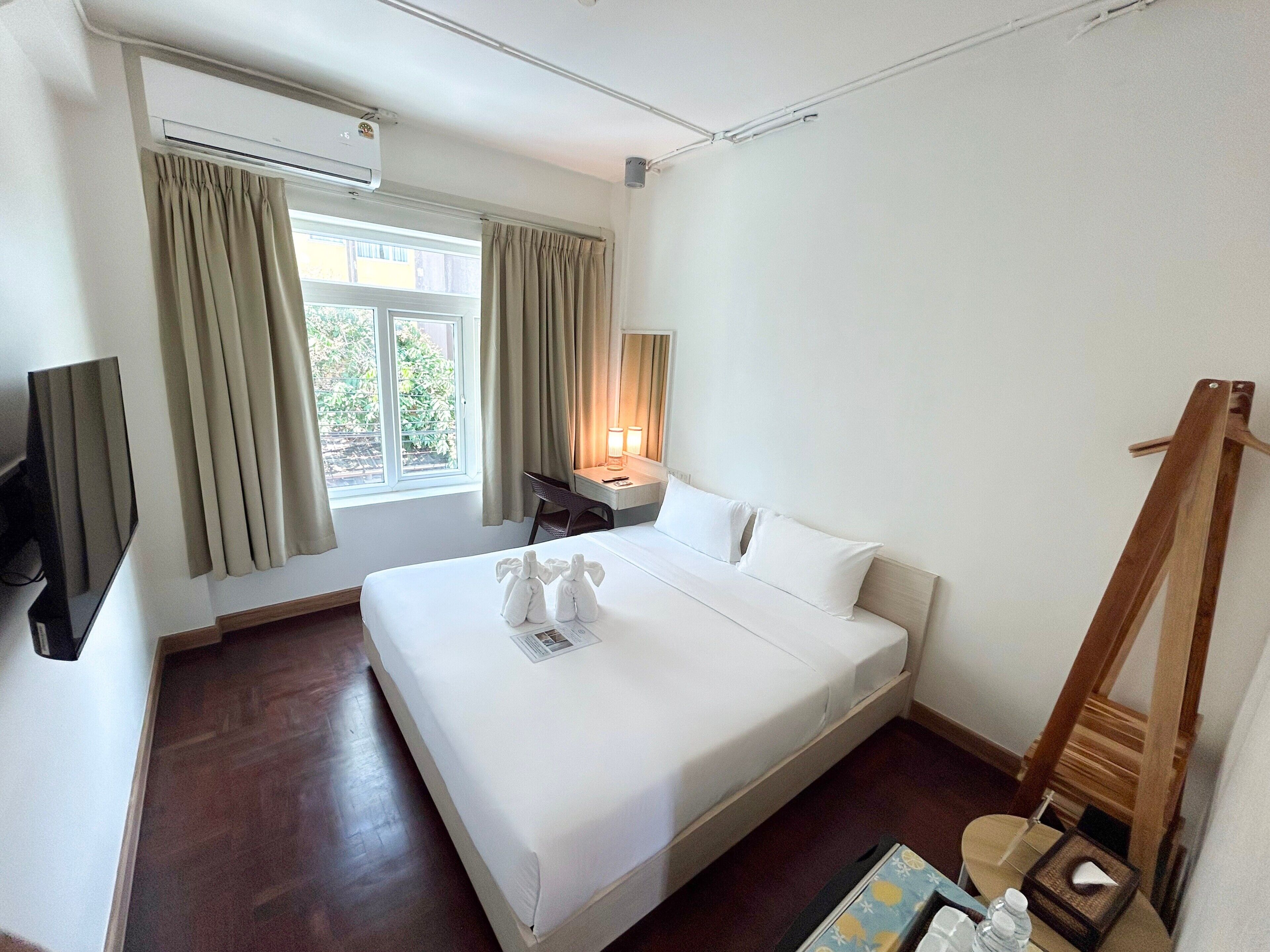 A hotel room with a bed, a desk, a chair, a TV, and a window with curtains.