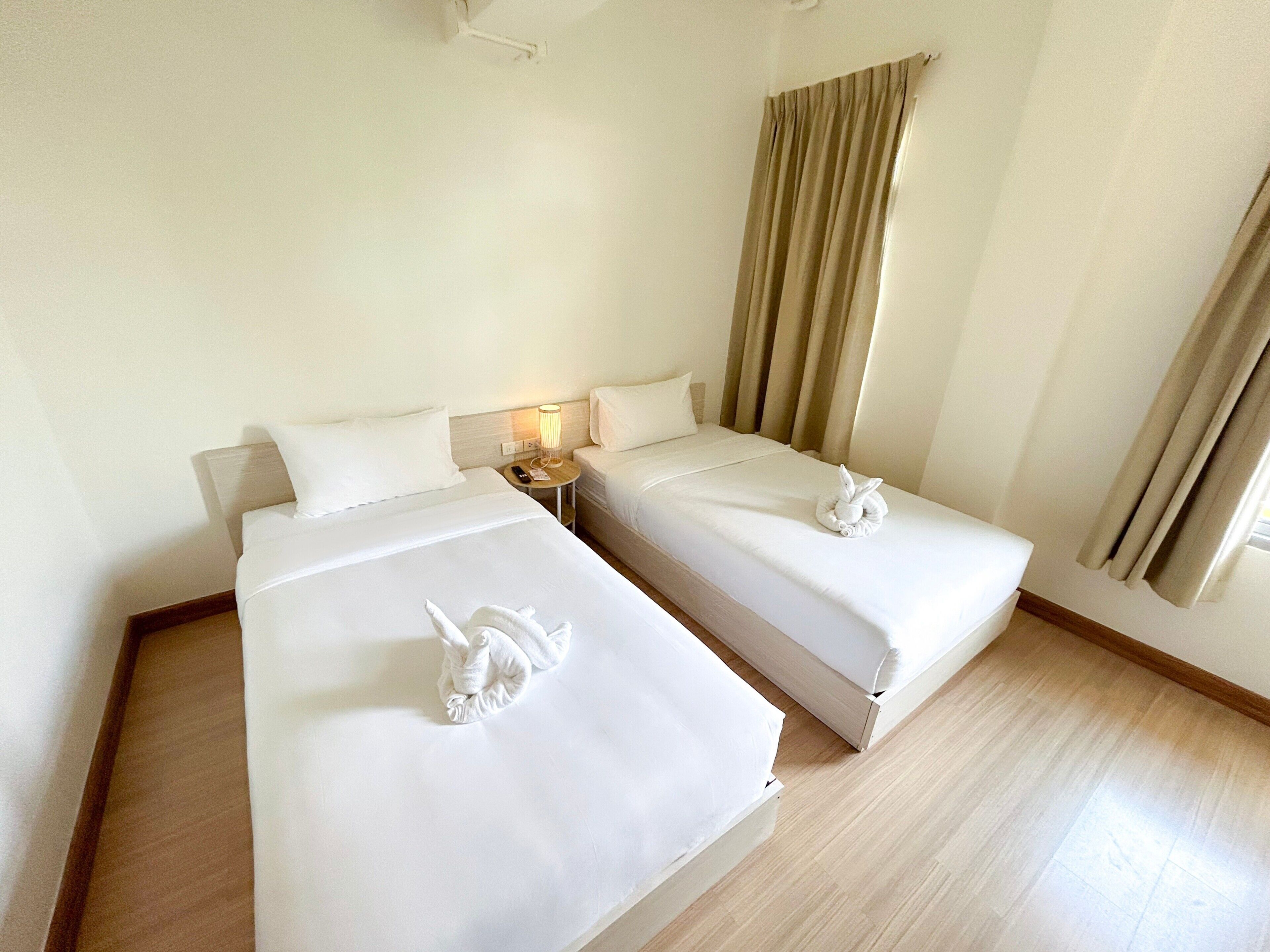 A hotel room with two beds, a nightstand with a lamp, and a window with curtains.