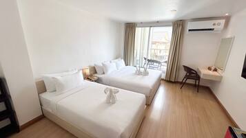 Ein Hotelzimmer mit zwei Betten, einem Schreibtisch, einem Stuhl, einer Klimaanlage und einem Fenster mit Vorhängen.