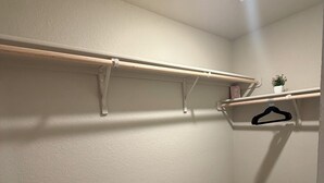 A corner closet with built-in shelves and a hanging rack, a ceiling vent, and a small potted plant. - Contemporary 3BR Home Near Base Fast Wi-Fi, Smart TV, Coffee Station (Killeen)