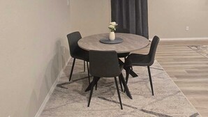 A dining area with a round table, four chairs, a vase with flowers, a patterned rug, and a dark curtain. - Contemporary 3BR Home Near Base Fast Wi-Fi, Smart TV, Coffee Station (Killeen)