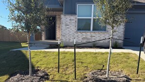 A residential area with a house, a well-maintained lawn, and two young trees planted in raised beds. - Contemporary 3BR Home Near Base Fast Wi-Fi, Smart TV, Coffee Station (Killeen)