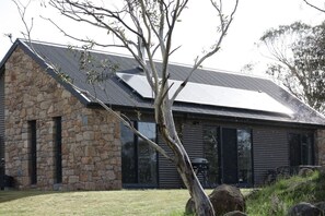 A modern house with a stone facade, large windows, and a sloped metal roof. - Emu`s Rest at Touchdown Cottages (Jindabyne)