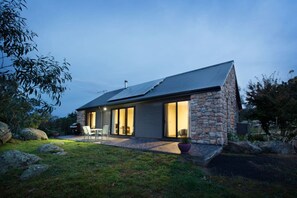 A modern house with a stone exterior, large sliding glass doors, and a patio with outdoor furniture. - Brumbies Run Touchdown Cottages (Jindabyne)