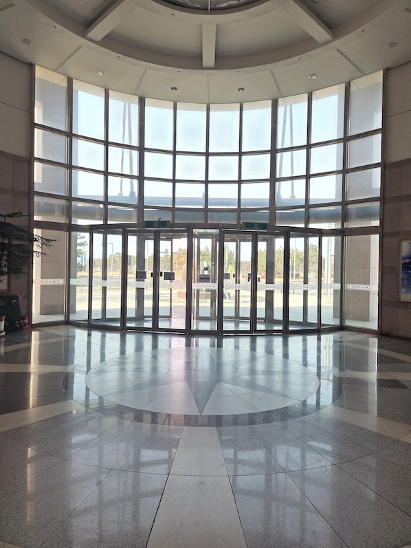 A spacious lobby with a curved ceiling, large windows, and a tiled floor.