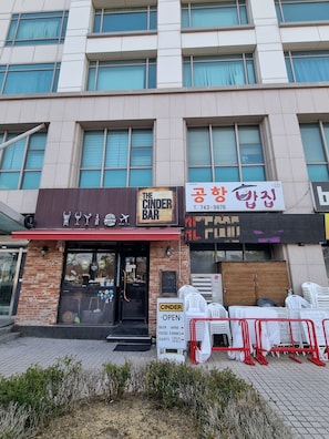 A building with a bar named 'The Cinder Bar' and a sign for '공항아파트' with a contact number.