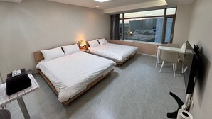 A hotel room with two beds, a desk, a chair, a window with a city view, and a ceiling light. - Incheon Airport Line Guest House (Incheon)