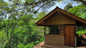 A small wooden cabin with a brick wall and a wooden door, surrounded by lush greenery. - OZ Cabin by Farmstay Managel (Cianjur)