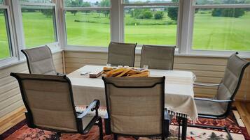 Un espace repas comprenant une table, des chaises et une vue sur un paysage verdoyant, visible à travers de grandes fenêtres.