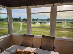 A room with a table, chairs, and large windows overlooking a grassy field.