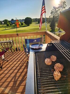 A barbecue grill with meat on it, a flag, and a view of a golf course.
