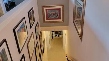 Un escalier orné de tableaux encadrés le long des murs, menant à une chambre à coucher avec un lit et une fenêtre.