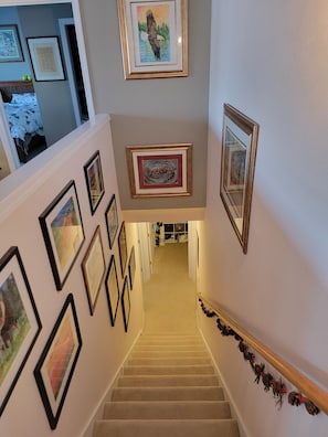 A staircase with framed artwork on the walls, leading to a bedroom with a bed and a window.