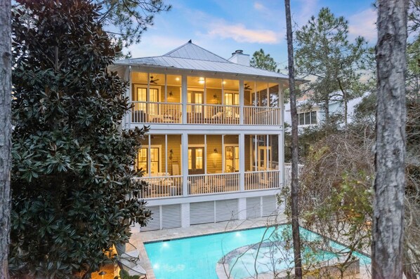 Une maison à deux étages dotée d’un balcon, d’une piscine et offrant une vue sur les arbres environnants.