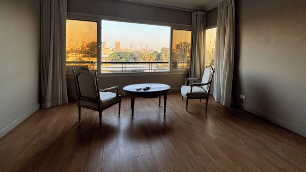 A room with a large window, two chairs, a small table, and a view of a cityscape. - Cosy Nile view Rowers 3 bedroom condo (Giza Governorate)
