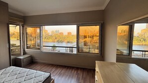 A bedroom with a large window, a bed, a nightstand, and a wooden dresser. - Cosy Nile view Rowers 3 bedroom condo (Giza Governorate)
