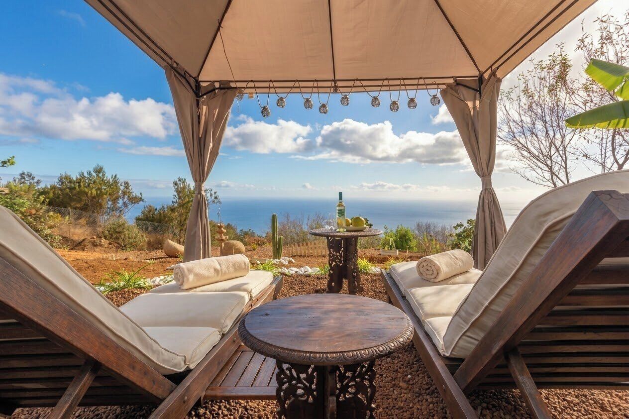 Un espacio de estar al aire libre techado con dos sillones reclinables y una mesa pequeña, con vistas a un paisaje pintoresco.