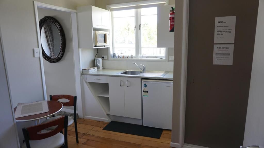 Cocina compacta con armarios blancos, microondas, fregadero y un pequeño comedor con mesa y sillas.