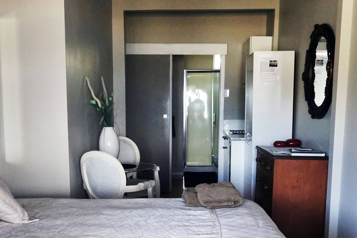 Un dormitorio con una cama grande, un aparador de madera, una silla, una mesita y un espejo.