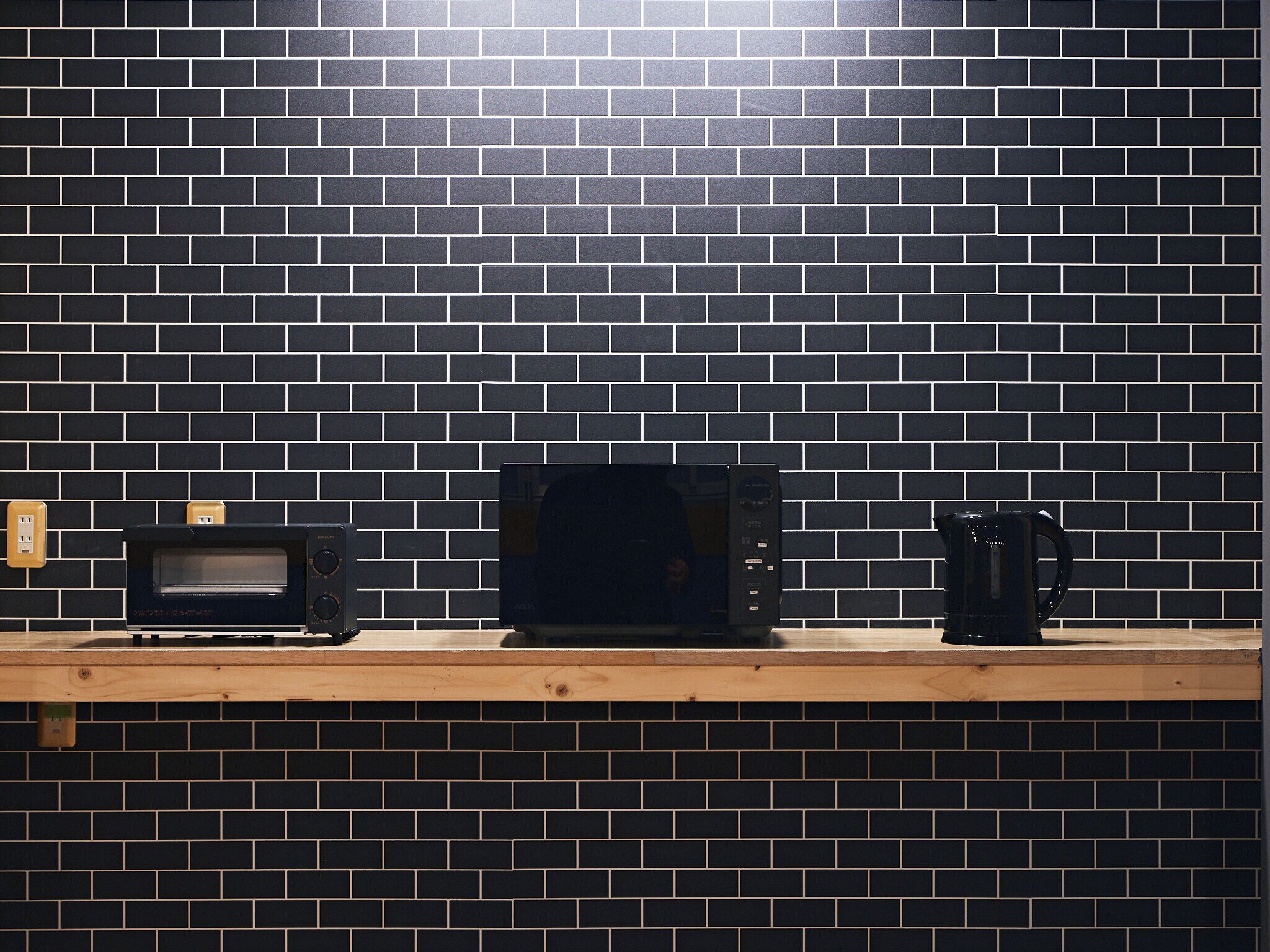 A kitchen with a black tiled backsplash, a microwave, and a coffee maker on a wooden countertop.
