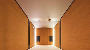 A narrow, modern hotel room with wooden walls, a bed, and two wall-mounted speakers. - Shijo Guesthouse HIVE - Hostel  (Kyoto)