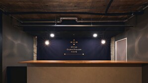 A reception desk with a dark wall, three spotlights, and a wooden floor. - Shijo Guesthouse HIVE - Hostel  (Kyoto)