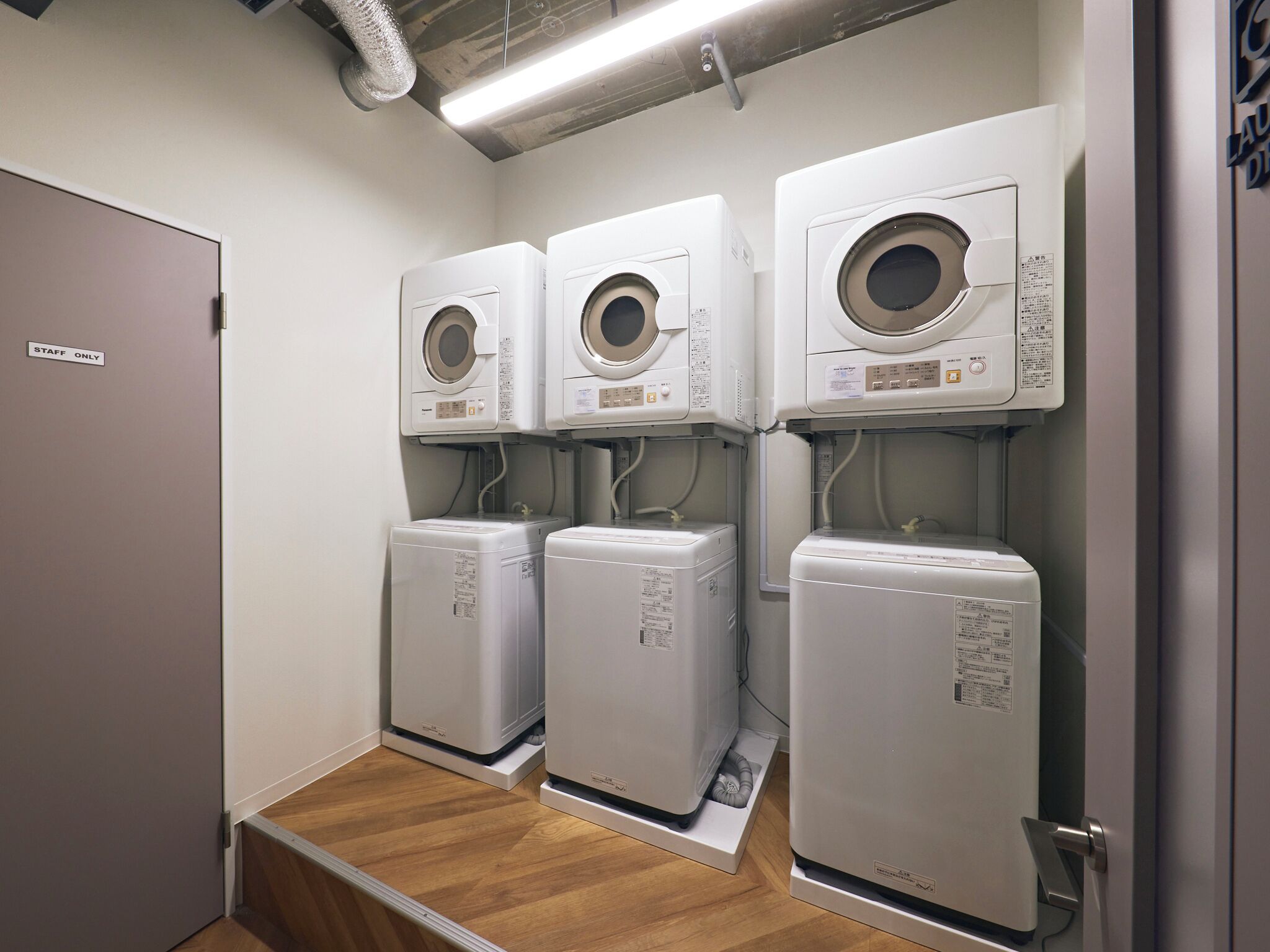 A laundry room with three stacked washing machines and a 'STAFF ONLY' sign on the door.
