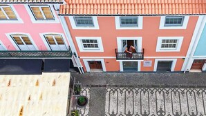 Un edifici de diversos pisos amb teulada de rajola vermella, un balcó amb una persona i un paviment amb dibuixos.