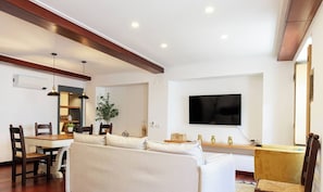 A modern living room with a sofa, dining table, chairs, a TV, and a plant.