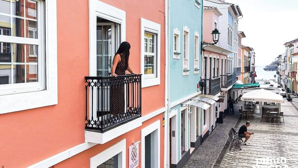 Un carrer estret amb edificis de colors, una dona a un balcó i una persona asseguda a terra.