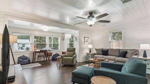 A spacious living room with a large sofa, a television, and a ceiling fan. - The Big Salty -Mid South SSI (St. Simons Island)