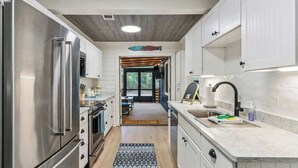 A modern kitchen with white cabinetry, stainless steel appliances, and a wooden ceiling. - The Big Salty -Mid South SSI (St. Simons Island)
