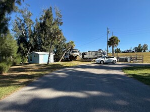 Un barrio residencial con una casa azul pequeña, un coche blanco y un camión grande estacionados en la calle.