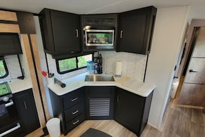 Una cocina compacta con muebles oscuros, un microondas y un lavamanos.