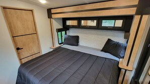 Ein kleines Schlafzimmer mit Bett, Kissen, einer Holztür und einem Fenster.