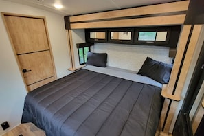 Ein kleines Schlafzimmer mit Bett, Kissen, einer Holztür und einem Fenster.