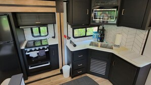 A compact RV kitchen with a stove, oven, microwave, and sink. - Myakka Cove Glamping (Venice)