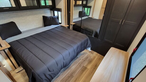 A compact bedroom with a bed, a small table, and a wardrobe. - Myakka Cove Glamping (Venice)
