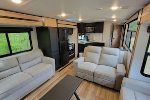 Interior compacto de una caravana con kitchenette, dos sofás y una mesita.