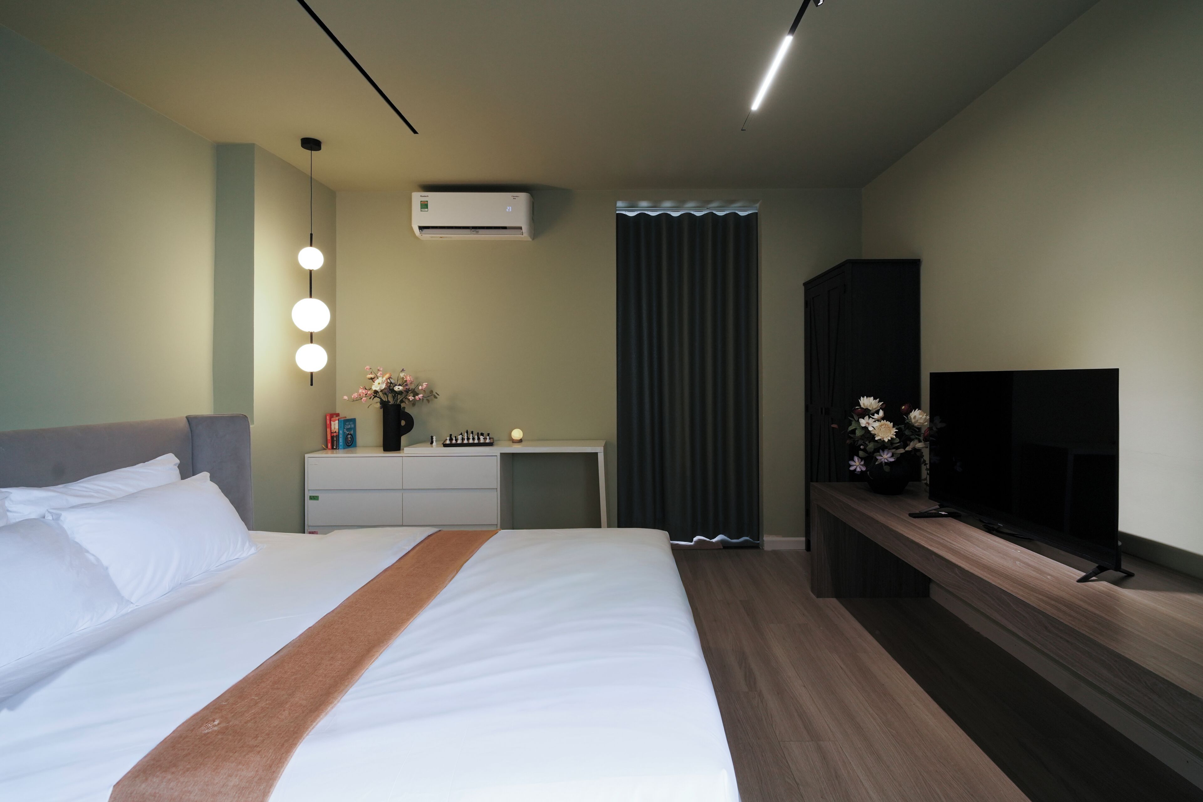 A hotel room with a bed, bedside table, TV, and an air conditioning unit.