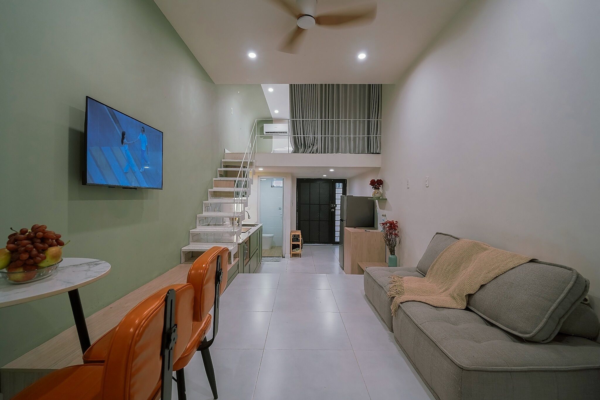 A modern living space with a dining area, a sofa, a TV, and a staircase leading to an upper level.