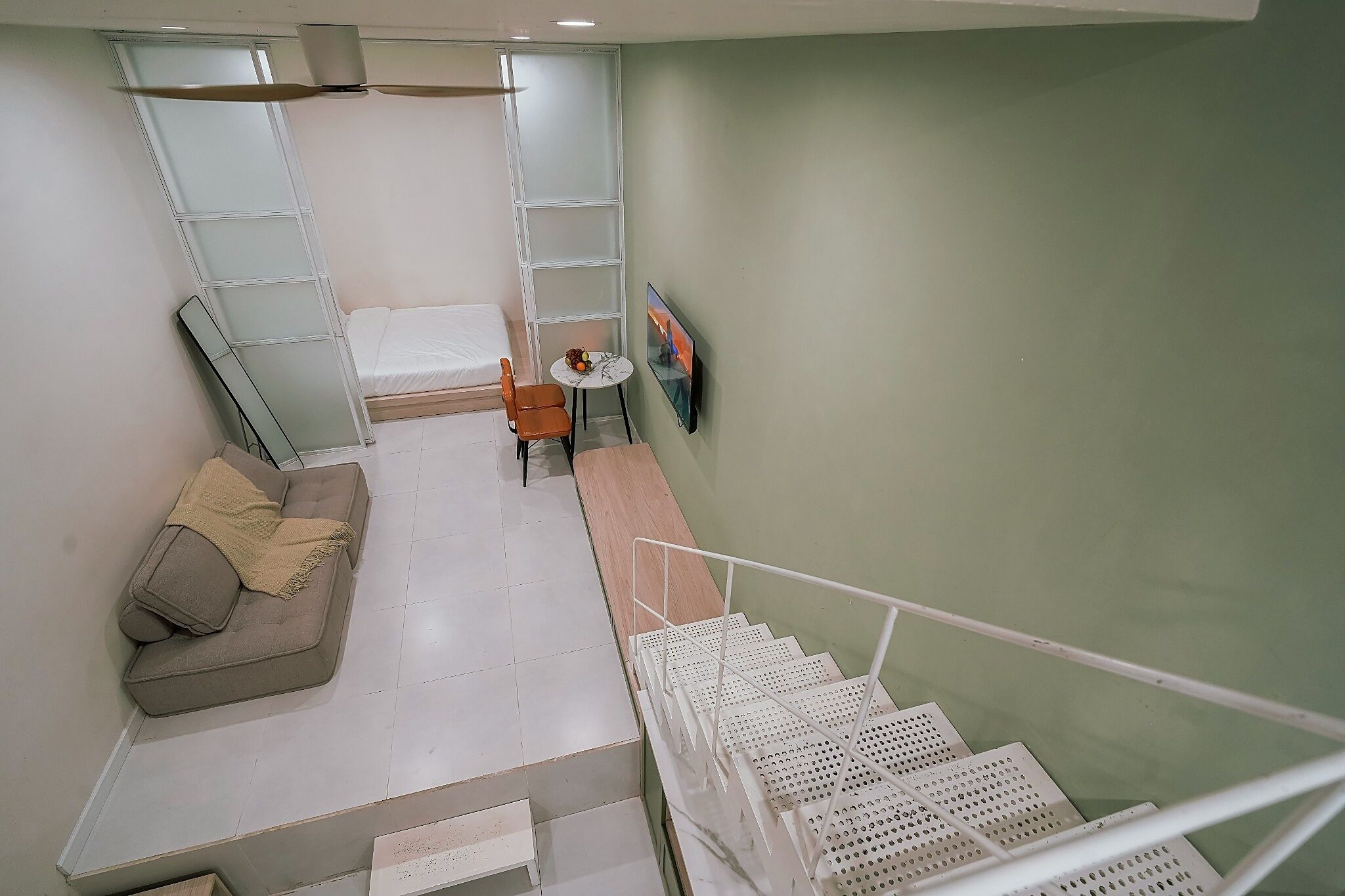 A room with a sofa, a small table with a fruit bowl, a TV, and a staircase with white railings.