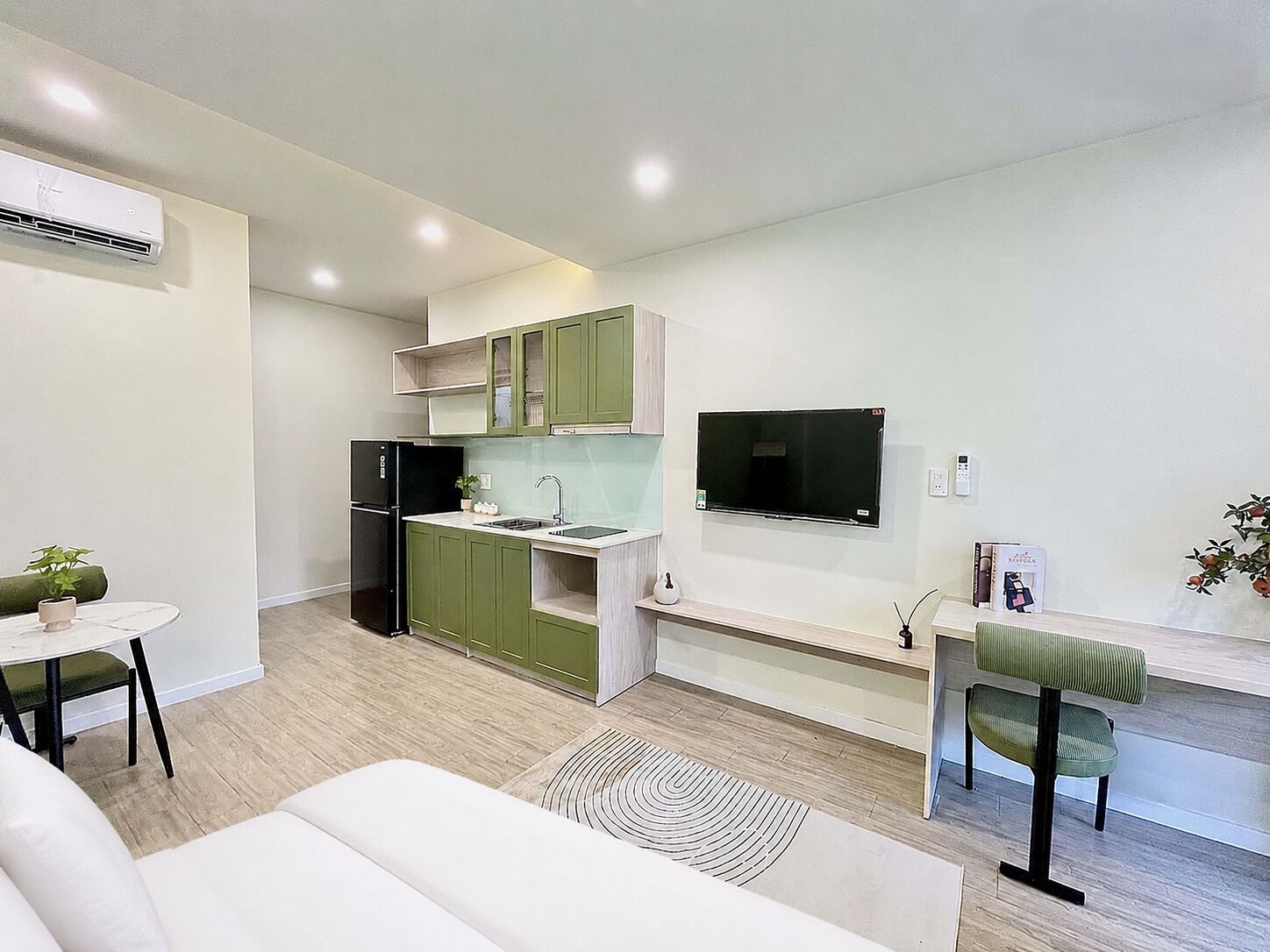 A modern kitchen with green cabinets, a black refrigerator, and a flat-screen TV mounted on the wall.