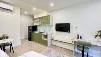 A modern kitchen with green cabinets, a black refrigerator, and a flat-screen TV mounted on the wall.