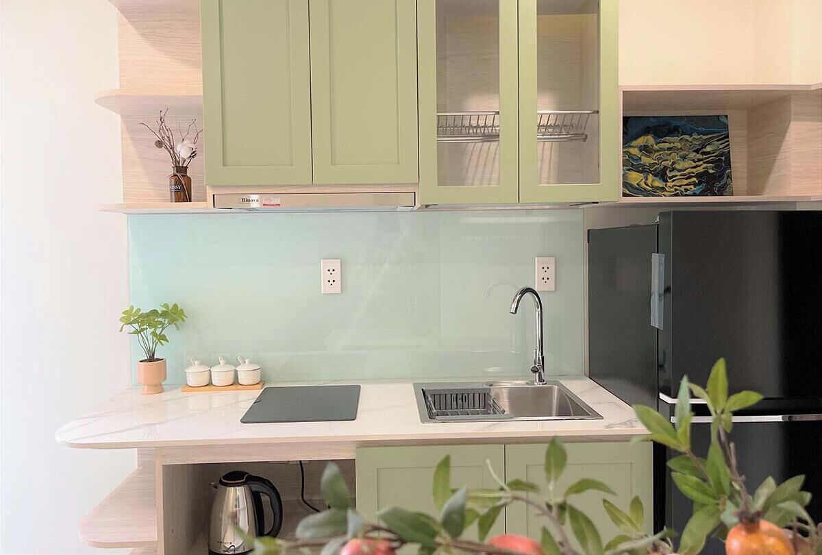 A modern kitchen with light green cabinets, a black refrigerator, and a stainless steel sink.