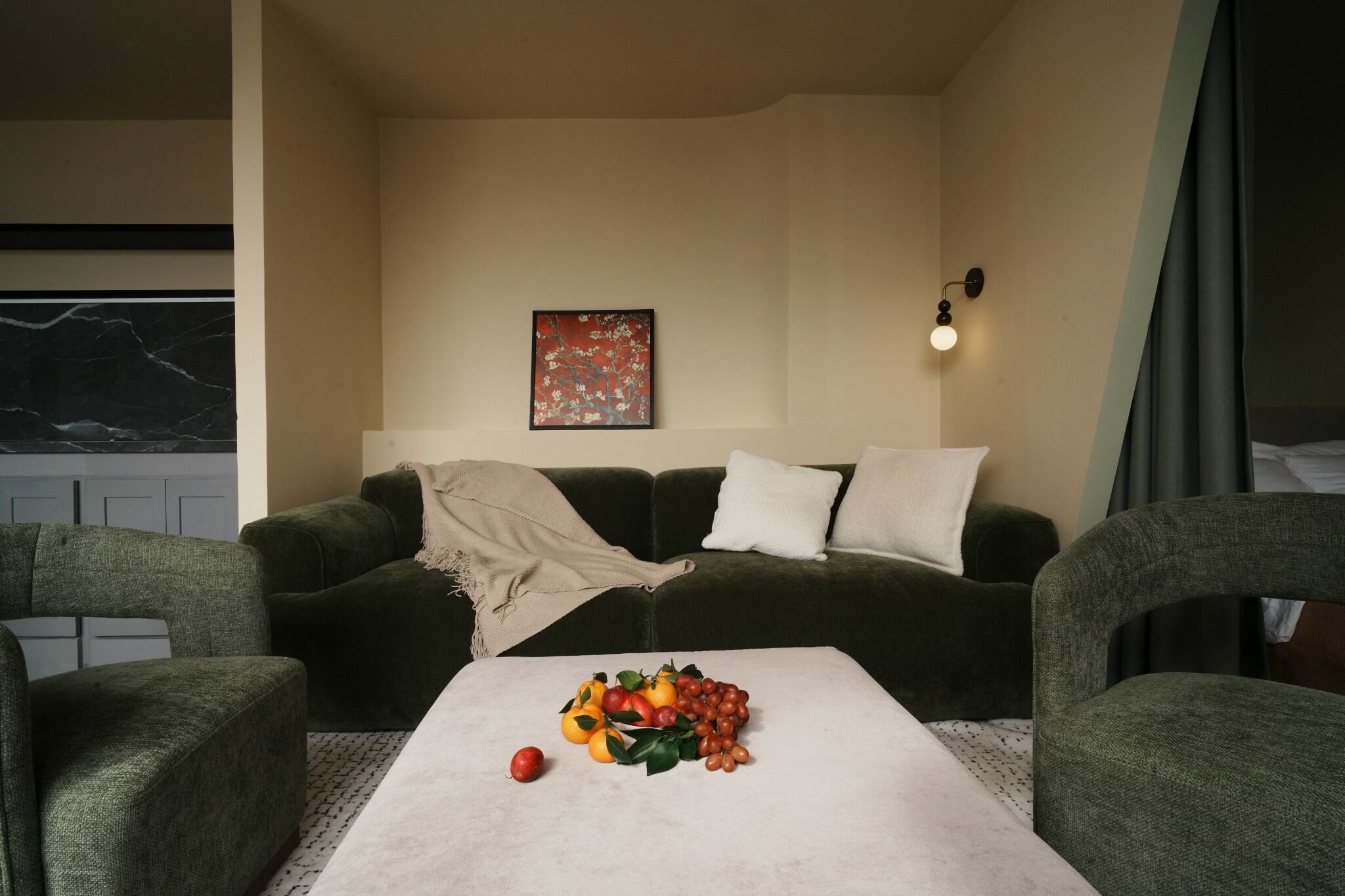 A living room with a sofa, a coffee table with fruit, a painting, and a wall-mounted light.