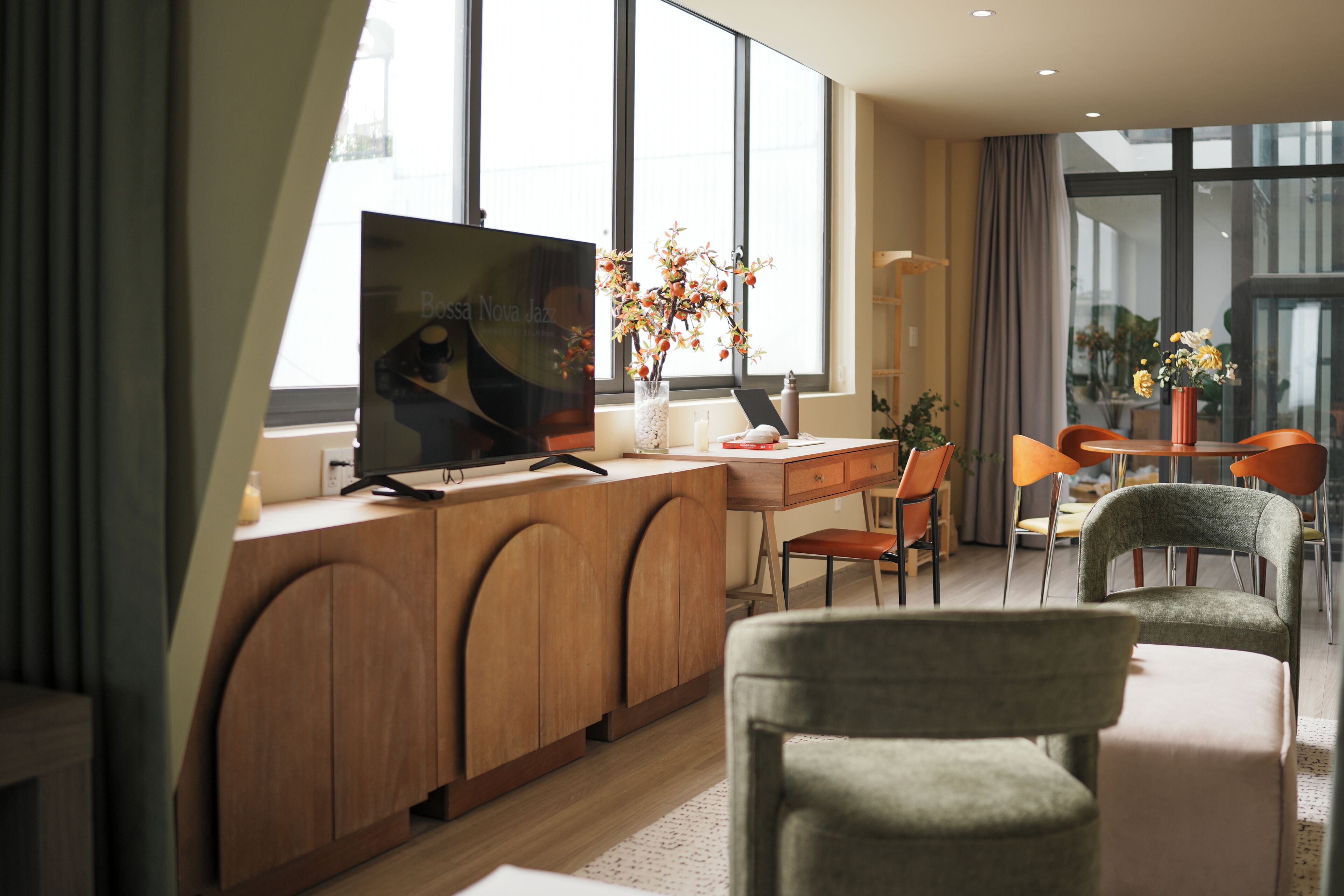 A modern hotel room with a large flat-screen TV, wooden furniture, and a view through large windows.